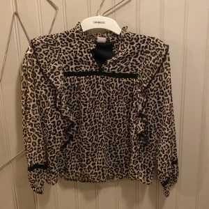 Leopardmönstrad blus från Lindex - Säljer en super fin leopardmönstrad blus från Lindex med volangdetaljer längs axlar och bröst. Blusen har hög krage, lång ärm och svarta banddetaljer vid ärmslut . Inget fel använd ca 2 gånger otroligt fin!!❤️❤️