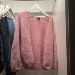 Rosa stickad kofta från Lindex - Mysig och fluffig rosa stickad kofta från Lindex i storlek XS/S. Koftan har en öppen front och långärmade, lite puffiga ärmar. Perfekt för att ge din outfit en soft och chill vibe. Passar dig som gillar ljusa färger och skönt material.