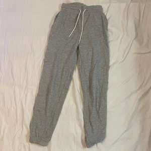 Grå mjukisbyxor från HM - Grå mjukisbyxor med elastisk midja och vit snörning. Byxorna har en avslappnad passform och är perfekta för chill dagar. Tillverkade i mjukt bomullsmaterial och har resår vid bensluten för extra komfort.