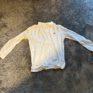 Långärmad Ralph Lauren pike - Vit långärmad pikétröja från Ralph Lauren med klassisk krage och den ikoniska loggan broderad på bröstet. Tröjan är i mjuk bomull och har en stilren look som passar perfekt till jeans eller chinos.