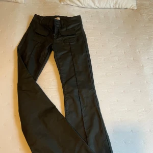 Svarta cargopants från Nelly - Svarta cargopants från Nelly med hög midja, raka ben och snygga fickor framtill med lock. Byxorna har dubbla knappar och dragkedja i gylfen. Materialet är slätt och ger en cool look, perfekt för dig som gillar streetstyle.