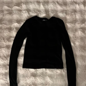 Svart ribbad tröja från FB Sister - En svart, ribbad långärmad tröja från FB Sister. Tröjan har en klassisk rund halsringning och är figurnära i modellen. Perfekt att matcha med jeans eller kjol för en clean look.