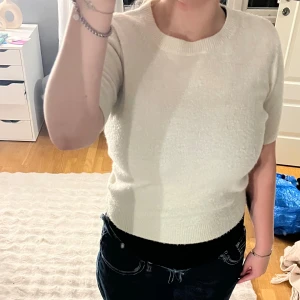 Vit stickad kortärmad tröja H&M - Superfin vit stickad tröja från H&M med korta ärmar och rund hals. Tröjan har en enkel och clean look med ribbade detaljer vid hals, ärmslut och nederkant. Perfekt att styla med jeans eller kjol för en fräsch vibe.