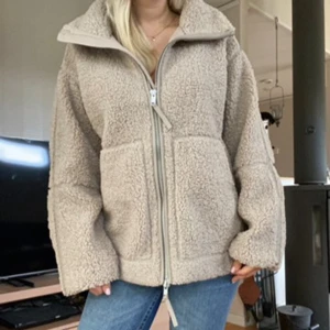Beige hm pilejacka  - Virala hm pilejacka i den beige färgen. Helt slutsåld. Prislapp kvar. Mysig beige teddyjacka med hög krage och två stora fickor framtill. Jackan har en rejäl dragkedja och är tillverkad i fluffigt fleece-material. Passformen är loose och ärmarna är långa, perfekt för kyliga dagar. Jag är 163 cm för referens 