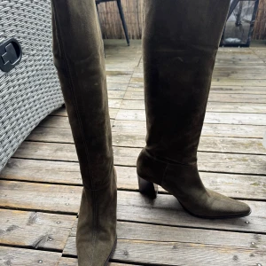 Mossgröna mockastövlar med klack - Snygga höga stövlar i mossgrön mocka med spetsig tå och stabil klack. Stövlarna har en elegant och tidlös design som passar perfekt till höst- och vinterlooken. Materialet är mjukt och ger en lyxig känsla. Endast använda vid ett enstaka tillfälle. Nyskick!