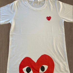 Comme des Garçons PLAY T-shirt - Comme des Garçons PLAY T-shirt  Beskrivning: Säljer en helt ny och oanvänd Comme des Garçons PLAY t-shirt. Den ikoniska designen med det röda hjärtat med ögon ger en unik och lekfull touch till din outfit. Perfekt för både avslappnade och mer stilmedvetna tillfällen.  *   Märke: Comme des Garçons PLAY *   Storlek: Medium *   Skick: Oanvänd, i perfekt skick *   Nypris: ca 1000 SEK  Missa inte chansen att äga denna eftertraktade t-shirt till ett bra pris! Kontakta mig gärna vid frågor.