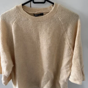 Beige stickad tröja från Gina Tricot - Mysig beige stickad tröja från Gina Tricot med rund halsringning och ribbade muddar. Tröjan har en enkel och stilren design, perfekt för lager-på-lager och passar till många olika outfits.