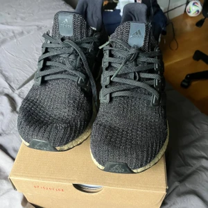 Adidas Ultra Boost svarta sneakers - Svarta Adidas Ultra Boost sneakers med stickad ovandel och klassisk Boost-sula i vitt. Skorna har snörning och detaljer i plast längs sidorna. Perfekta för dig som gillar streetwear och vill ha bekväma skor med snygg design. Storlek 44 2/3 men är små i storleken så mer som 43