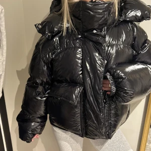 Svart glansig pufferjacka med huva - Säljer en svart pufferjacka med glansig finish och stor, mysig huva. Passformen är oversized och den är perfekt för kalla dagar. Använd några gånger men är i jättebra skick. Så snygg och väldigt varm. säljer då jag måste rensa lite jackor😅 kan sänka vid snabb affär!!💗