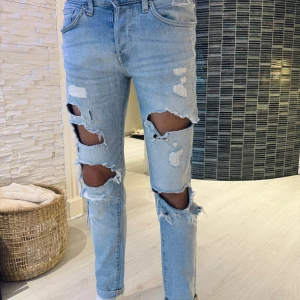 Ljusblå skinny jeans med stora hål - Riktigt snygga ljusblå skinny jeans med stora slitningar och hål framtill på båda benen. Jeansen har klassisk femficksdesign och är tillverkade i denim. Perfekta för dig som gillar en edgy och trendig look.