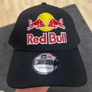 Red Bull keps från New Era 9FORTY - Snygg svart Red Bull keps från New Era 9FORTY med broderad logga framtill och mesh på sidorna och bak. Justerbar passform med snapback-spänne. Kepsen har detaljer i rött, gult och vitt och är perfekt för dig som gillar motorsport och streetstyle.