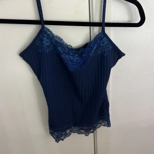 Marinblå spetsdetaljerad linnetopp Romwe - Snygg marinblå linnetopp i storlek XS. Toppen har tunna axelband, ribbad struktur och vackra spetsdetaljer med blommönster vid halsringning och nederkant. Perfekt för dig som gillar feminina och trendiga detaljer.