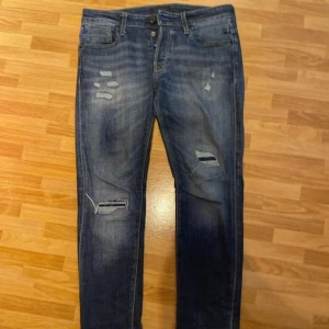 Jack & Jones jeans - Snygga blå jeans från Jack & Jones, modell Slim Glenn. Jeansen har slitna detaljer och hål på benen för en trendig look. De är slim fit med klassisk femficksdesign och har en mörk tvätt med ljusa partier. Perfekta för dig som gillar en avslappnad men stilren stil.