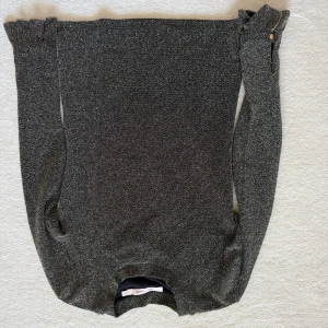 Glittrig svart tröja Rue de Femme - Säljer en svart glittrig tröja från Rue de Femme i storlek S. Tröjan har långärmade ärmar med volangdetalj och guldig knapp vid ärmslutet. Materialet är glittrigt och ger en lyxig känsla. Perfekt för dig som vill sticka ut med stil.