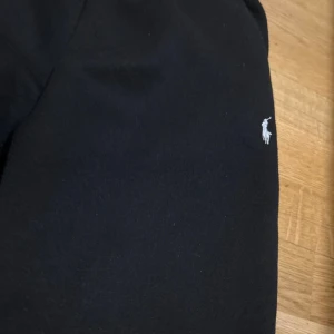 Svarta mjukisbyxor från Polo Ralph Lauren - Svarta mjukisbyxor från Polo Ralph Lauren med klassisk vit broderad logga på benet. Byxorna har resår i midjan med snörning och raka ben. Perfekta för chill eller streetwear. Tillverkade i mjukt bomullsmaterial för extra komfort.