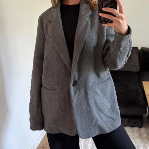 Grå kavaj från Noisy May - Säljer en grå kavaj från Noisy May i oversized modell. Kavajen har klassisk krage, en knapp framtill och två fickor. Materialet är mjukt och känns lite ulligt, perfekt för lager-på-lager. Enkel att styla med både jeans och kjol.