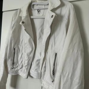 Vit jeansjacka med dragkedjor - Snygg vit jeansjacka i storlek 164. Jackan har coola silverfärgade dragkedjor både framtill och vid ärmsluten, samt klassisk krage och croppad passform. Perfekt för dig som gillar stilrena detaljer och vill ha en jacka som sticker ut.