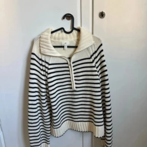Randig stickad tröja med half zip - Säljer en mysig stickad tröja från HM i vitt och svart med bred krage och half zip framtill. Tröjan har ett randigt mönster, ribbade muddar och långärmad passform. Perfekt för dig som gillar chill och snygg stil.