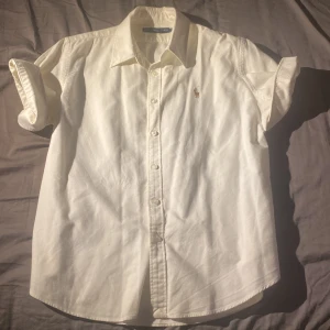 Vit kortärmad skjorta Ralph Lauren - Vit kortärmad skjorta från Ralph Lauren med klassisk krage och knäppning framtill. Skjortan har broderad logga på bröstet och är tillverkad i bomull, perfekt för en clean och stilren look.