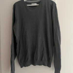Mörkgrå tröja från Pier One - En stilren mörkgrå tröja från Pier One i storlek L. Tröjan har rund halsringning, långa ärmar och ribbade muddar vid ärmslut och nederkant. Perfekt för lager-på-lager och enkel att matcha med olika outfits.