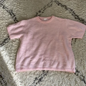 Ljusrosa stickad kortärmad tröja - Superfin ljusrosa stickad tröja med korta ärmar och rund hals. Perfekt för dig som gillar mjuka material och enkel stil. Tröjan har en clean look utan mönster eller detaljer, vilket gör den lätt att matcha med allt.