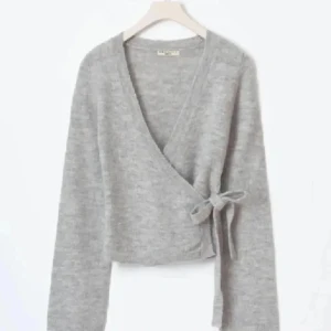 Grå omlottkofta med knyt - Superfin grå omlottkofta med knyt i sidan och v-ringad hals. Koftan är stickad och har långa ärmar, perfekt för lager-på-lager och chill dagar. Enkel att matcha med både jeans och kjol.