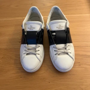 Valentino Garavani Rockstud Open Lace-Up Sneakers - Säljer ett par Valentino Garavani Open sneakers i vitt skinn med bred svart rem. Köpta på Cettire. 2025-03-19. Originalbox och allt följer med. 
