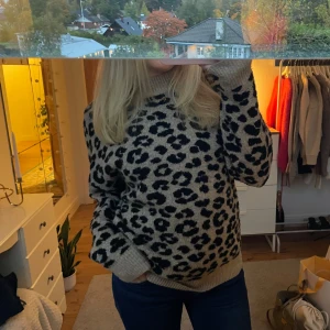 Beige leopardmönstrad stickad tröja - Säljer en supermysig stickad tröja i beige med svart leopardmönster. Tröjan har en relaxed fit, ribbade muddar och rund halsringning. Perfekt för att hålla sig varm och snygg under kyliga dagar.