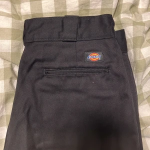 Svarta Dickies 874 byxor - Säljer ett par klassiska svarta Dickies 874 byxor med raka ben och breda hällor. Byxorna har en stilren look med Dickies-logga ovanför bakfickan. Helt nya då strl va för stor! 