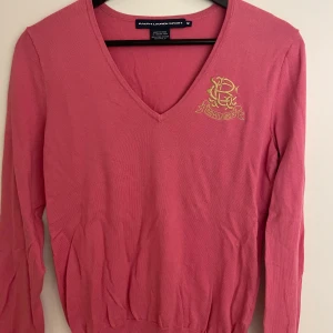 Rosa v-ringad tröja från Ralph Lauren - Rosa v-ringad tröja från Ralph Lauren Sport med broderad logga på bröstet. Tröjan är i 100% bomull, har långa ärmar och ribbad nederkant. Storlek M. Bra skick, inga defekter. 