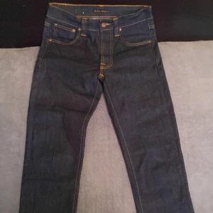 Nudie Jeans Lean Dean dry denim - Mörkblå Lean Dean jeans från Nudie Jeans med klassisk femficksdesign, kontrastsömmar och snygga broderade bakfickor. Tillverkade i 99% ekologisk bomull och 1% elastan för en bekväm passform. Slimmad, rak siluett och ikonisk logga på bakfickan.