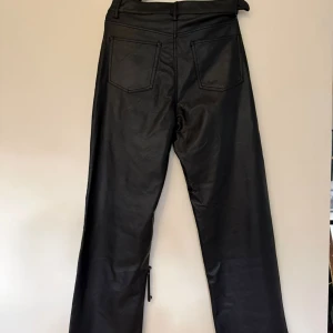 Svarta skinnbyxor från H&M, strl 44 - Snygga svarta byxor i skinnimitation från H&M i storlek 44. Byxorna har raka ben, klassisk femficksmodell och dragkedja med knapp framtill. Skulle säga att byxorna är mer 40 än 44. Litet märke på bakfickan.