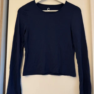 Mörkblå långärmad topp från Cubus - Säljer en stilren mörkblå långärmad topp från Cubus i mjuk bomull. Modellen är croppad med rund halsringning och har en liten slits vid ärmslutet för extra edge. Perfekt att matcha med jeans eller kjol för en clean look.