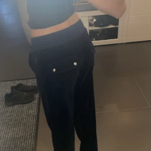 Mörkblå sammetsmjukisbyxor med snörning - Säljer ett par mörkblå mjukisbyxor i sammet med bred resår i midjan och snörning framtill. Byxorna har raka ben och fickor med knappdetaljer bak. Perfekta för en chill och snygg look. råka köpa för stor storlek endast använda när jag tog bilderna!