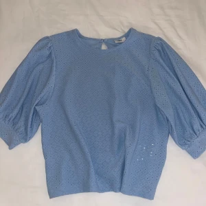 Ljusblå blus med puffärm från JDY - Säljer en ljusblå blus från JDY i storlek S. Blusen har broderade hålmönster över hela tyget, rund halsringning och en liten knapp i nacken. Puffiga trekvartsärmar med resår vid ärmslut ger en trendig look. Använd typ 2 gånger. ☺️🌸