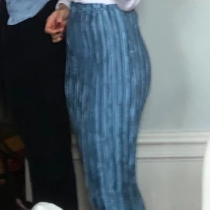 Blå kjol från Filippa Strandberg - Säljer en blå långkjol med vertikala ränder från Filippa Strandberg. Kjolen har en snygg plisserad look och är gjord i glansigt, mjukt material som känns lyxigt. Resår i midjan för skön passform. Perfekt för dig som gillar stilrena detaljer och vill sticka ut.