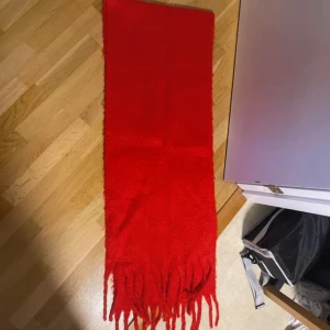 Röd halsduk med fransar - En enkel och snygg röd halsduk med långa fransar i ändarna. Halsduken är rektangulär och har en klassisk look som passar perfekt för kalla dagar. Perfekt accessoar för att liva upp vinteroutfiten.