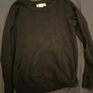 Svart stickad tröja med rund hals - En klassisk svart stickad tröja från Vila med rund halsringning och långa ärmar. Perfekt basplagg med ribbade muddar vid ärmslut och nederkant. Enkel och stilren design som passar till allt.