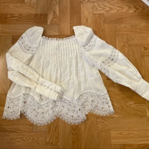 & Other stories blus med spets  - Créme vit blus med vackra spetsdetaljer och puffärmar. Klädda knappar vid ärmsluten och dekorativa broderier. Med knytning där bak Ger en söt, bohemisk eller romantisk look – perfekt till både jeans och kjol! Använd få gånger, i mycket fint skick. Material: Rami (naturmaterial) Nypris: ca 1000kr 