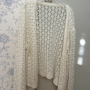 Vit virkad kofta i stickad bomull - Superfin vit kofta med virkat mönster och öppen front. Den är stickad i bomull och har långa ärmar samt en luftig, bohemisk känsla. 