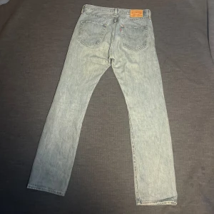 Levi's 501 ljusblå jeans straight fit - Klassiska Levi's 501 jeans i ljusblå tvätt med raka ben och femficksmodell. Jeansen har normal passform och är tillverkade i slitstarkt bomullsdenim. Perfekt för dig som gillar en tidlös och avslappnad look.