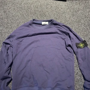 Stone Island sweatshirt - Säljer en marinblå sweatshirt från Stone Island med klassisk rund hals och ribbade muddar. Tröjan har den ikoniska Stone Island-patchen på vänster ärm och är gjord i mjuk bomull. Perfekt för dig som gillar streetwear och vill ha en clean look.