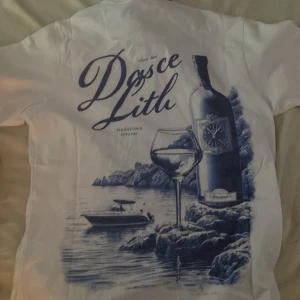 Vit t-shirt Leon Marcel med tryck XS - Har aldrig haft på den, fick den i fel storlek så säljer vidare här. Skick:Sprillans Nytt. Vit t-shirt från Leon Marcel i storlek XS. Framsidan har broderad text 'Marcel' i blått och baksidan har ett stort blått tryck med vinflaska, glas och båt vid klippor. Klassisk passform och rund hals. Snygg och stilren med coolt motiv. 