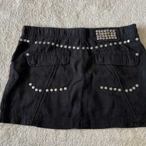 Minikjol med nitar - Cool y2k minikjol med nitar 🖤Riktigt punkig eller gothic 🥀Gammal Gina från tidigt 00-tal, har köpt secondhand! Storlek 42, som L 🥀Riktigt kort och kan funka på 38-40 om man vill ha lowrise 🖤Såååå cool och unik! Jättefint skick också 🖤Nitarna är dessutom i metall, inte plast, så ganska tunga! 