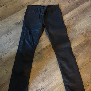 Svarta byxor från Jack & Jones 33/34 - Svarta byxor från Jack & Jones i modellen Ben Original Comfort. Klassisk femficksdesign, smal passform och knappgylf. Snygga och stilrena, perfekta till en streetwear-look. Materialet typ läder! Passar nog L