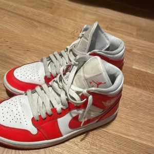 Nike Air Jordan 1 orange och vit - Säljer ett par Nike Air Jordan 1 i klassisk röd och vit färg. Skorna har högt skaft, snörning och den ikoniska Air Jordan-loggan på sidan. Ovandelen är i skinn med perforerad tå och röd yttersula. Perfekta för dig som vill sticka ut med en tidlös sneaker.