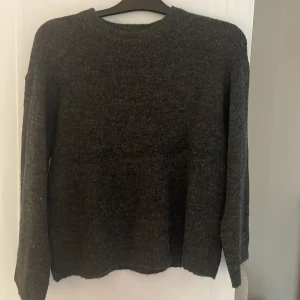 Mörkgrå stickad tröja från 157 XS - Mysig mörkgrå stickad tröja från 157 i storlek XS. Tröjan har rund halsringning, långa ärmar och en klassisk, enkel design som passar perfekt till lager-på-lager. Perfekt för kyliga dagar och enkel att matcha med jeans eller kjol.