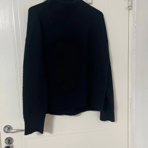 Svart stickad tröja från Kappahl - Svart stickad tröja från Kappahl i storlek S. Tröjan har en enkel och klassisk design med långärmade ärmar och rund hals. Materialet är en blandning av polyester, akryl, ull och elastan vilket gör den mjuk och bekväm. Perfekt för kyliga dagar.