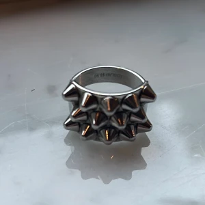 Silvrig ring med nitar från Edblad - Cool och chunky ring från Edblad i silvrig metall med två rader av utstickande nitar runt hela ringen. Perfekt för dig som gillar edgy och unik stil. Storlek 18.50, bred design som verkligen syns på handen.