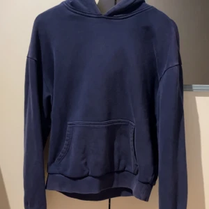 Mörkblå hoodie - En stilren mörkblå hoodie med tjockt tungt material som ger en premium känsla i plagget. Tröjan har långa ärmar och en relaxed passform, perfekt för chill outfits eller som lager under ex en overshirt. Tröjan är använd och man ser på hur tyget fadeat och slitits att den är använd men ännu i bra skick.